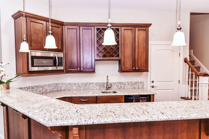 Wood and granite kitchen with pendant lights, built-in microwave, and wine rack cabinetry.